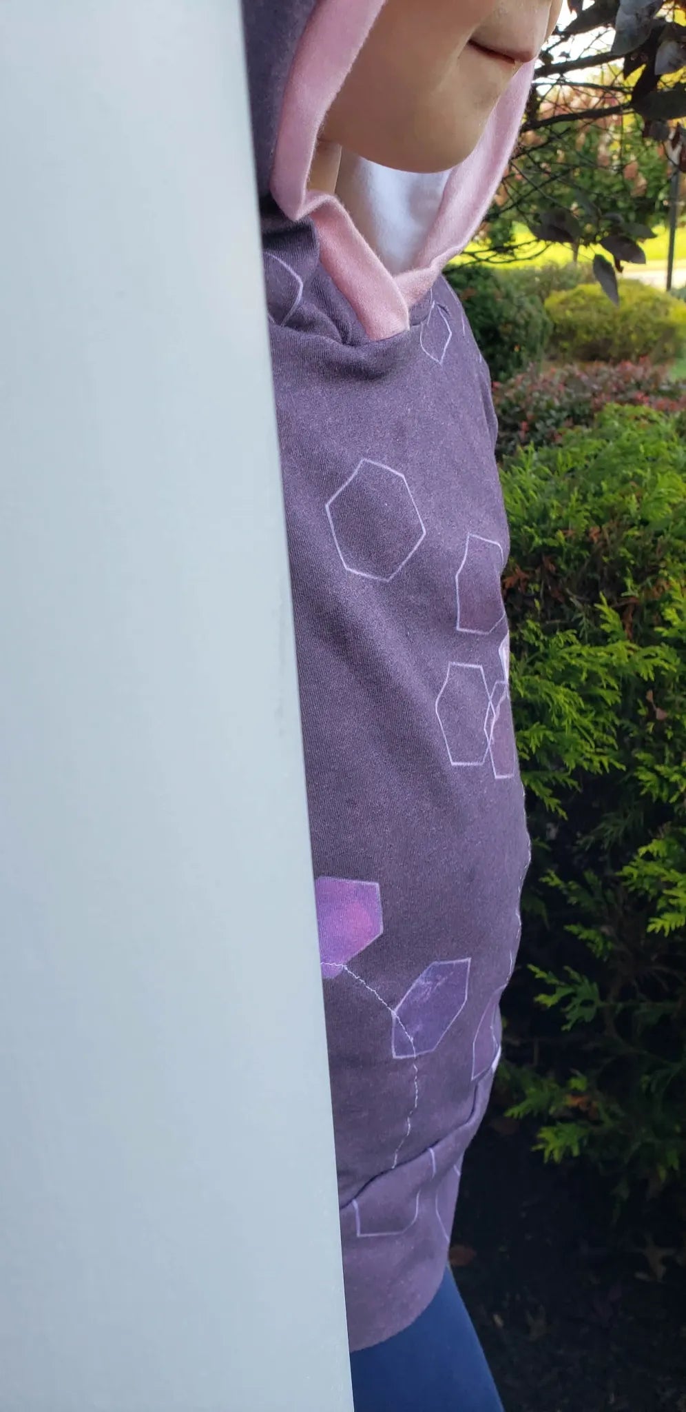 A person wearing a burgundy hoodie with a geometric pattern and pink lining.