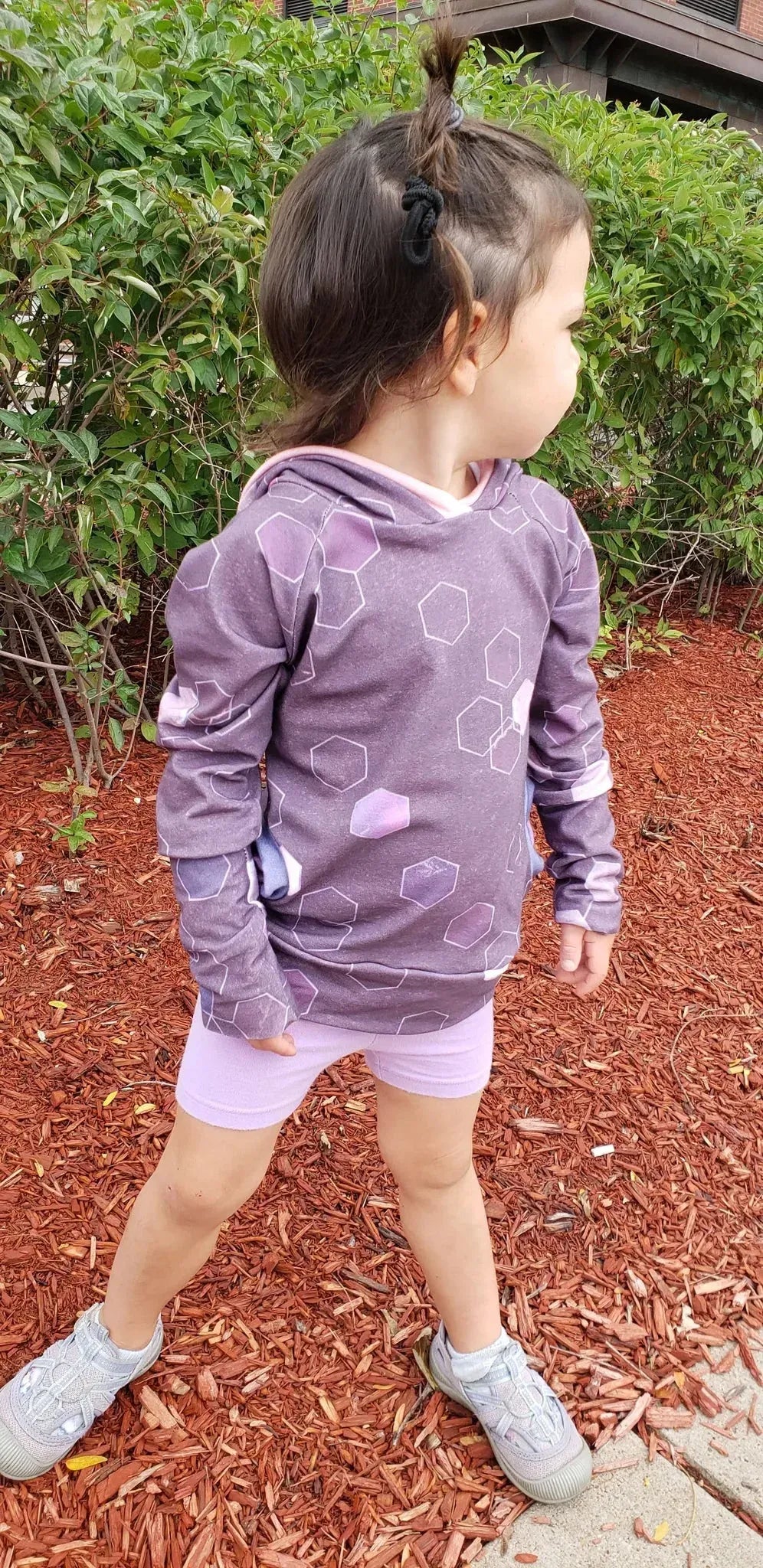 A child wears a burgundy geo print hoodie and light purple shorts.