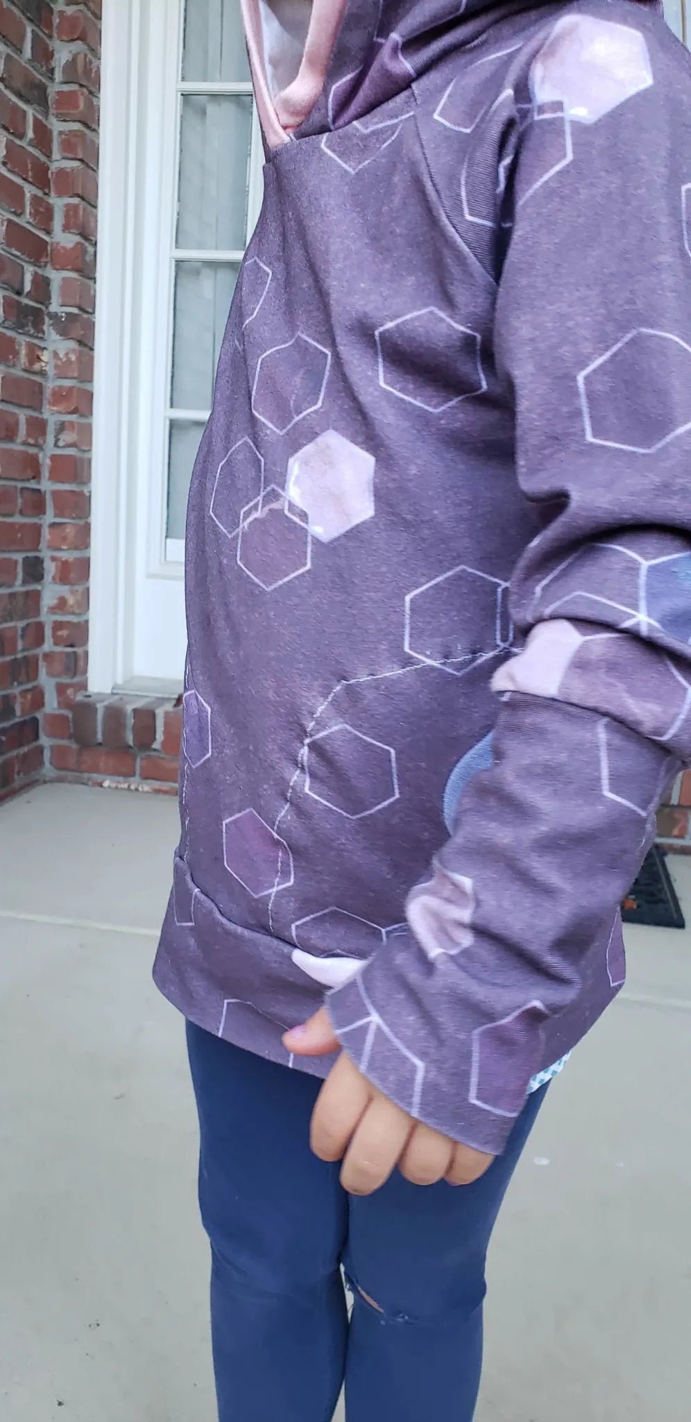 A child wears a burgundy hoodie with a geometric pattern and blue pants.