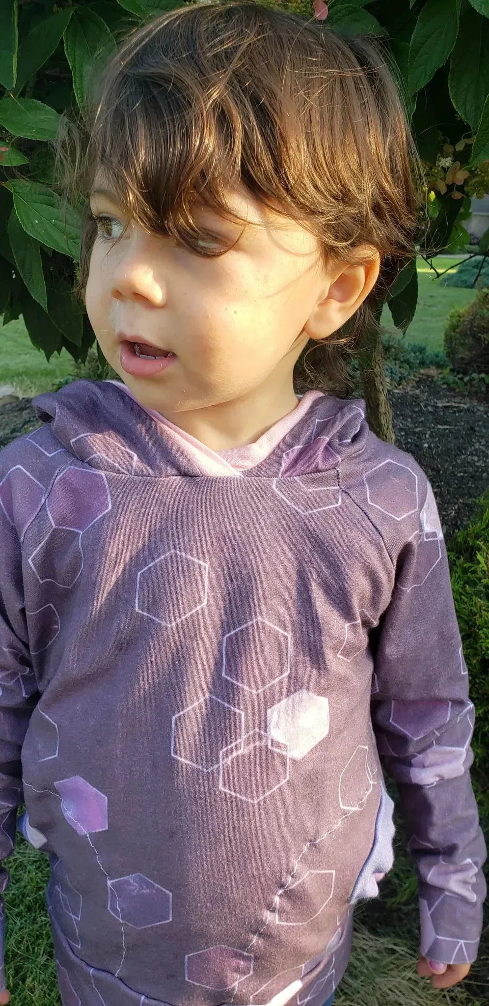 A child wears a burgundy hoodie with a geometric pattern.