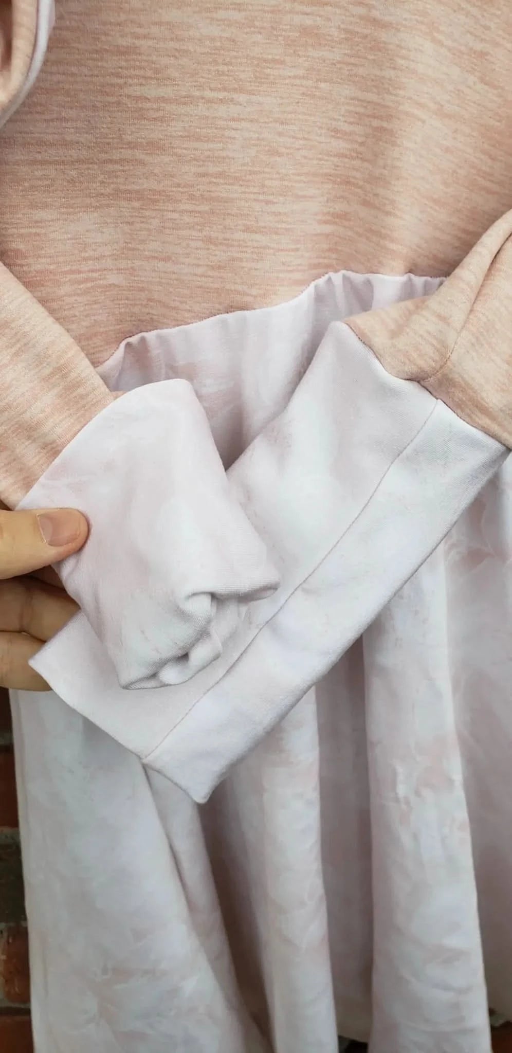 A person holds a light pink fabric with a subtle floral pattern.