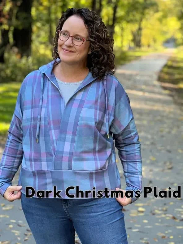 A woman wears a blue and purple plaid hoodie with jeans, standing on a path.