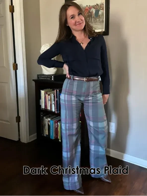 A woman models wide-leg plaid pants with a dark blue shirt and brown belt.