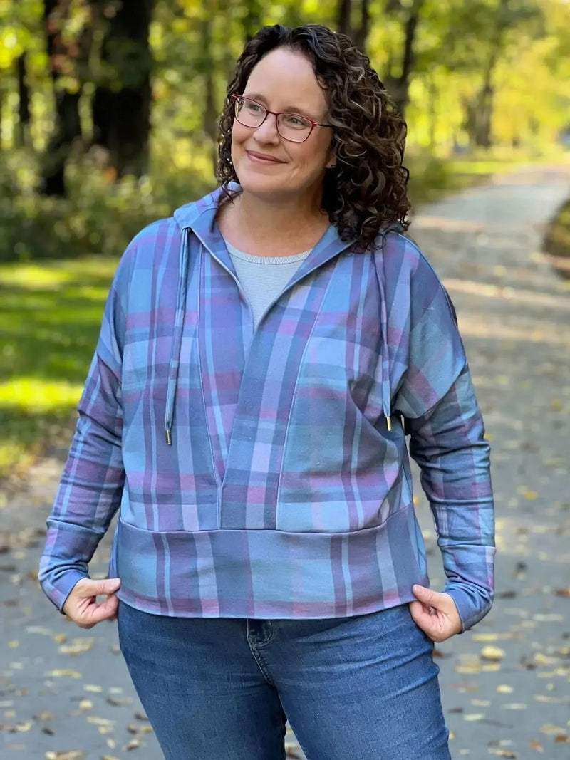 A woman wears a blue and purple plaid hoodie with jeans outdoors.
