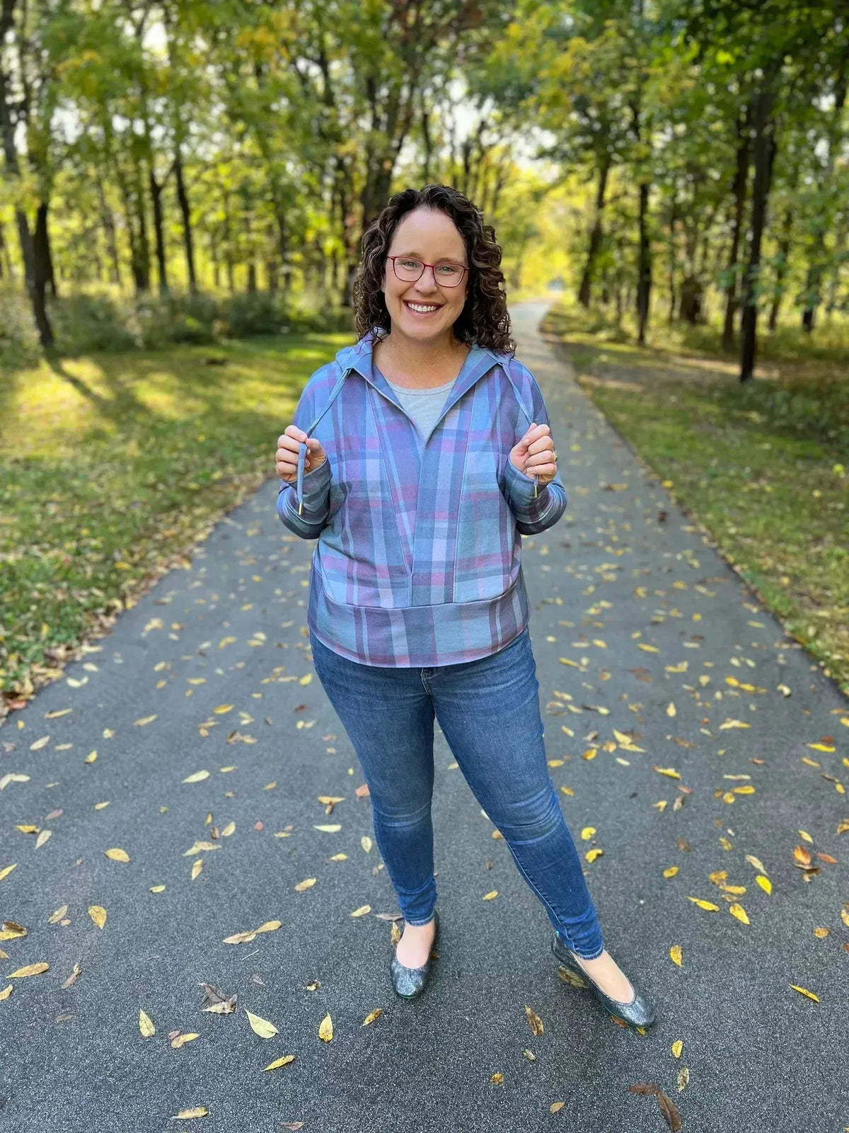Woman wearing a dark plaid shirt in green and pink on a wooded path.