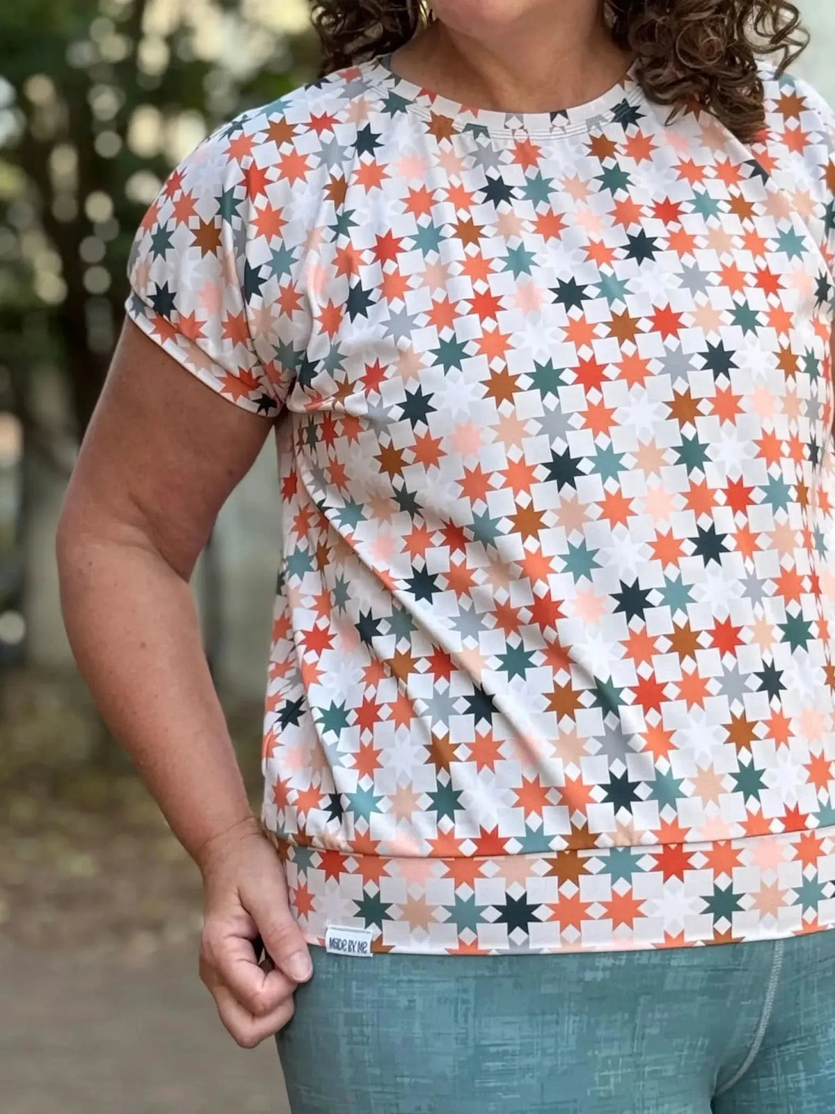Orange geometric star print fabric with multicolored accents on a white background.