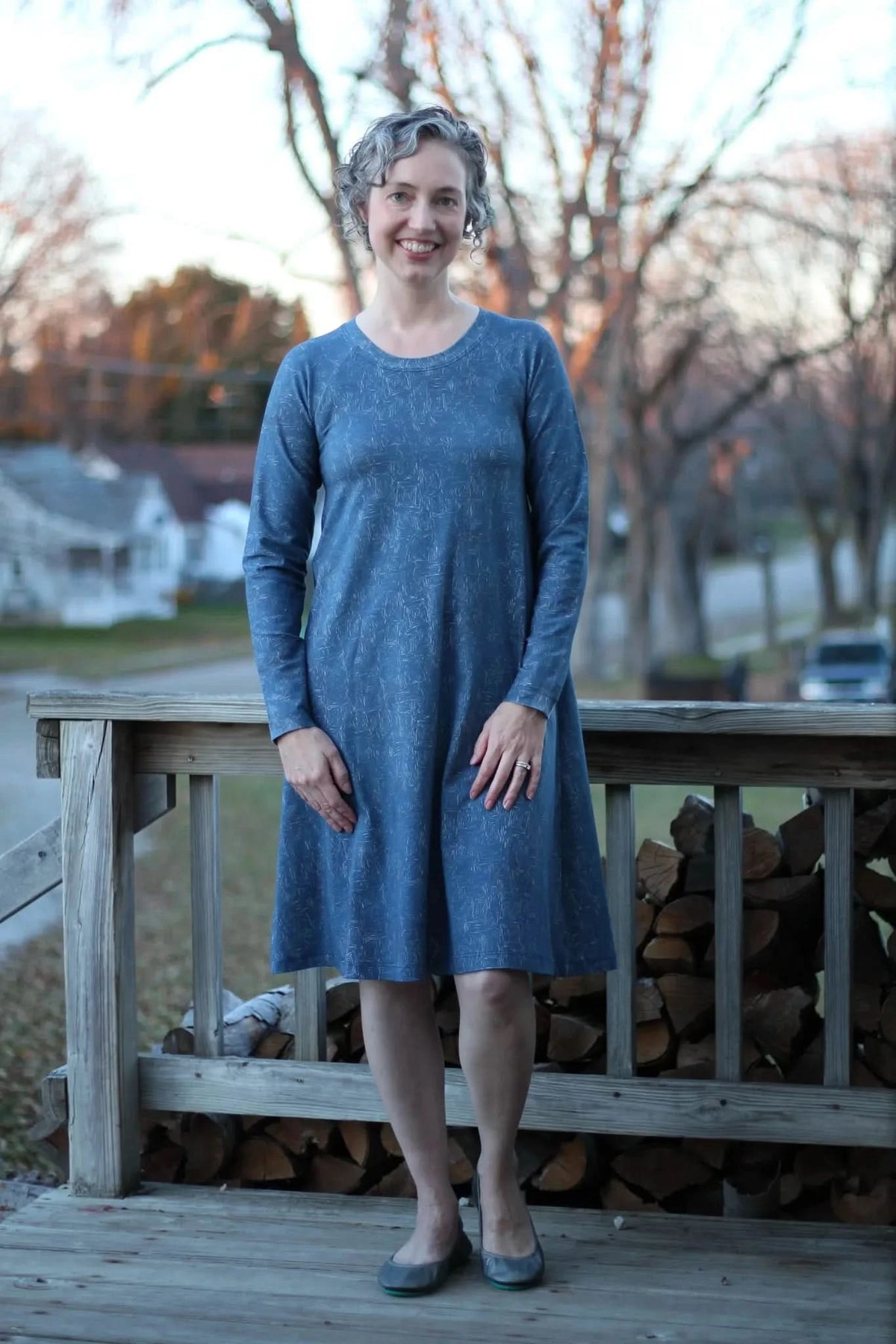 A woman in a blue dress with a subtle white geometric pattern stands on a wooden deck.