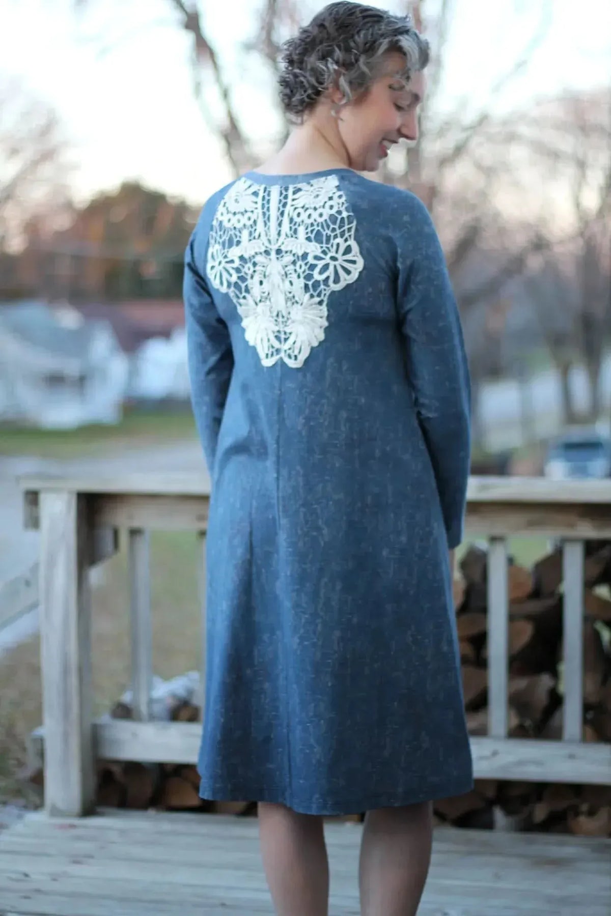 A woman in a blue dress with white lace on the back smiles over her shoulder.