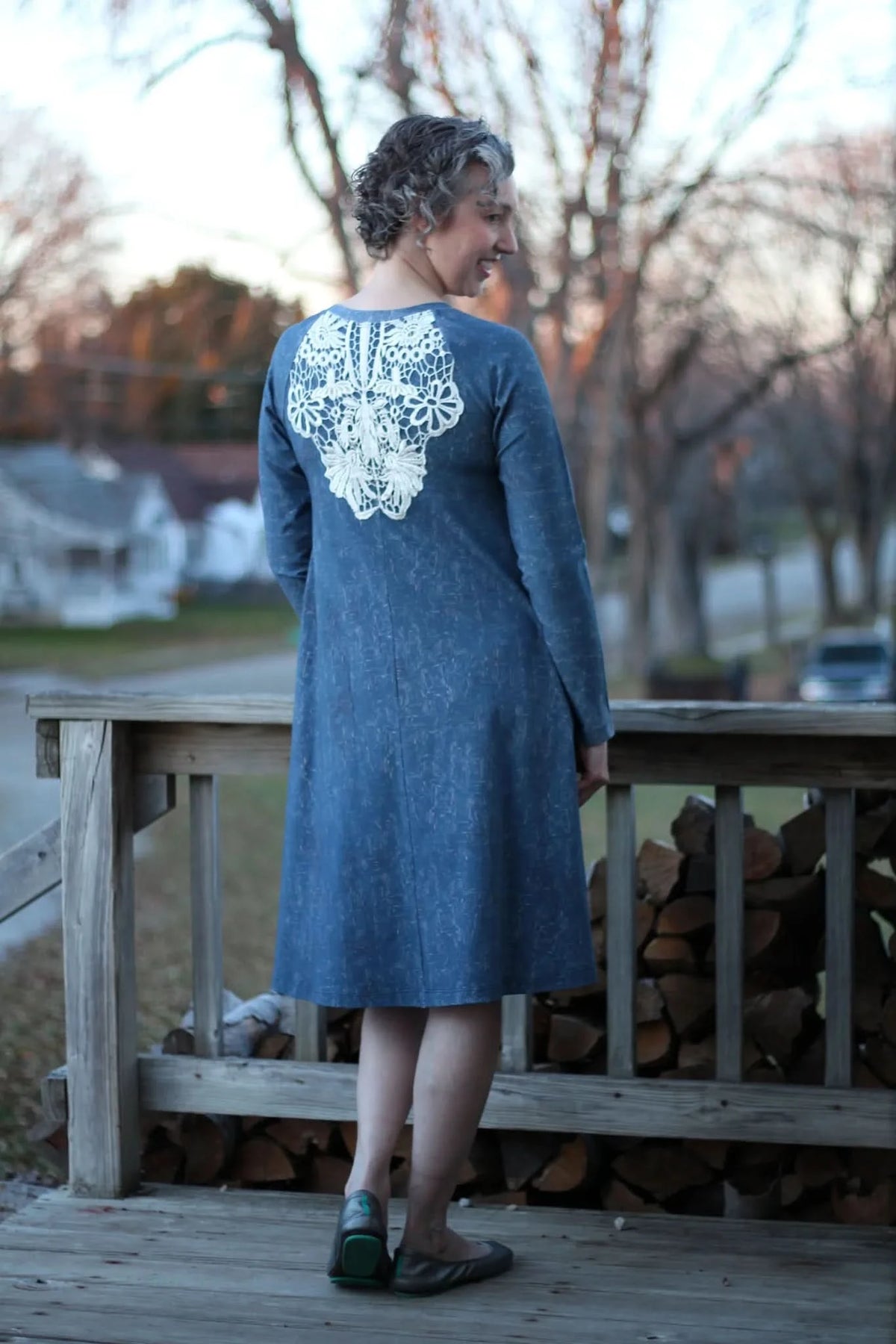 A woman in a blue dress with white lace on the back stands on a wooden deck.
