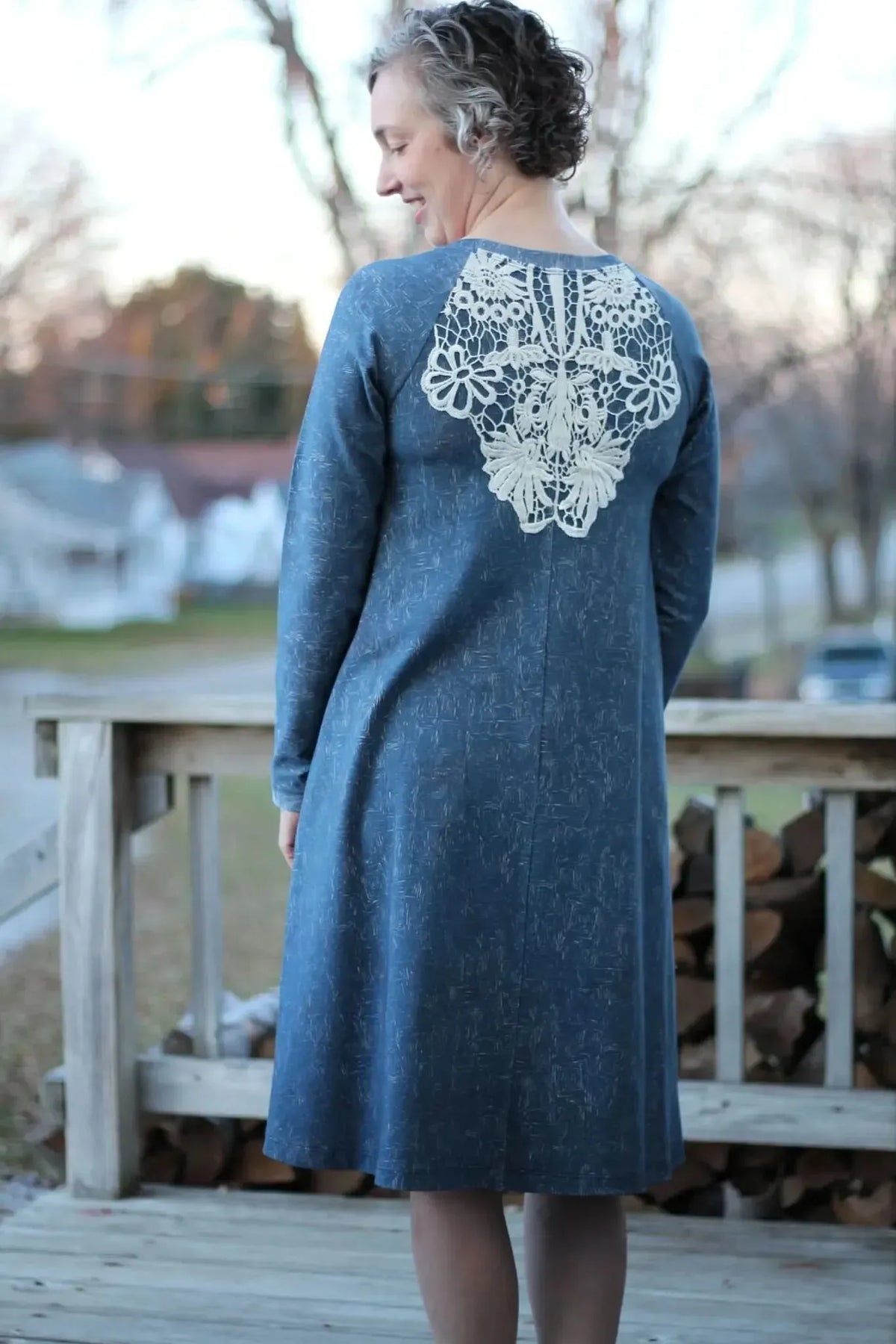 A woman in a blue dress with a white lace back stands on a wooden deck.