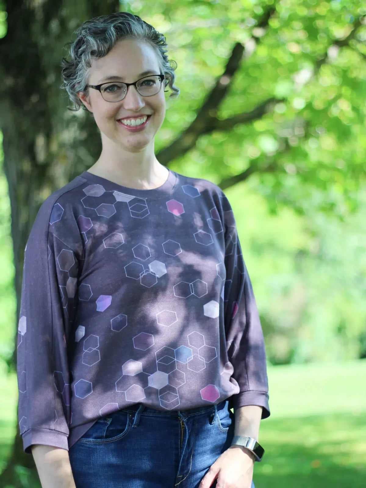 A woman wears a burgundy geo print long-sleeved shirt and blue jeans outdoors.