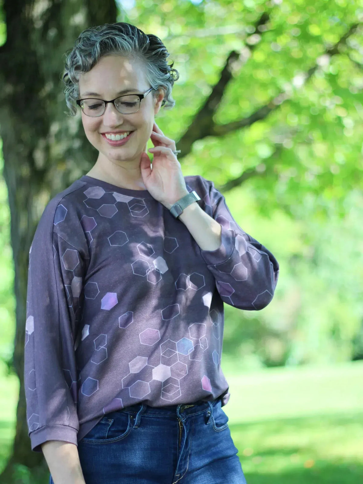 A woman wears a burgundy geo print long-sleeved top and blue jeans.