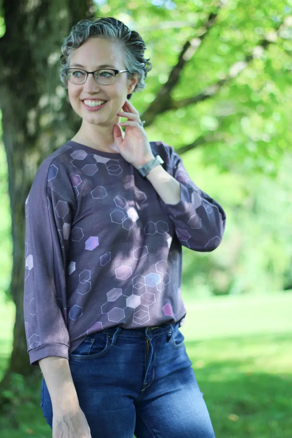 A woman smiles wearing a burgundy geo print long-sleeved shirt and jeans.