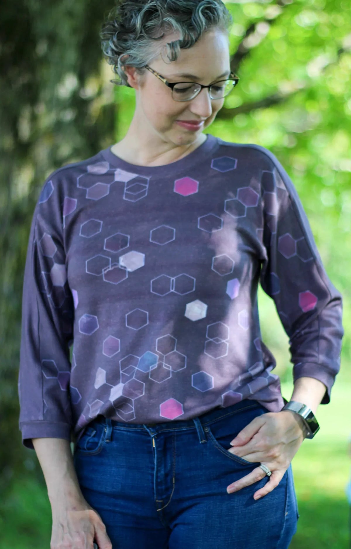 A woman wears a burgundy shirt with a geometric pattern and blue jeans.