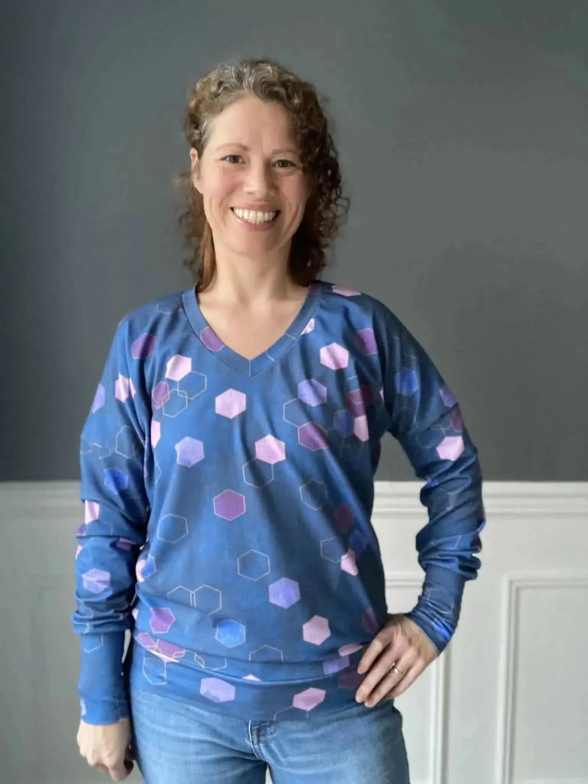 Woman wearing a blue long-sleeved shirt with purple and pink geometric patterns.