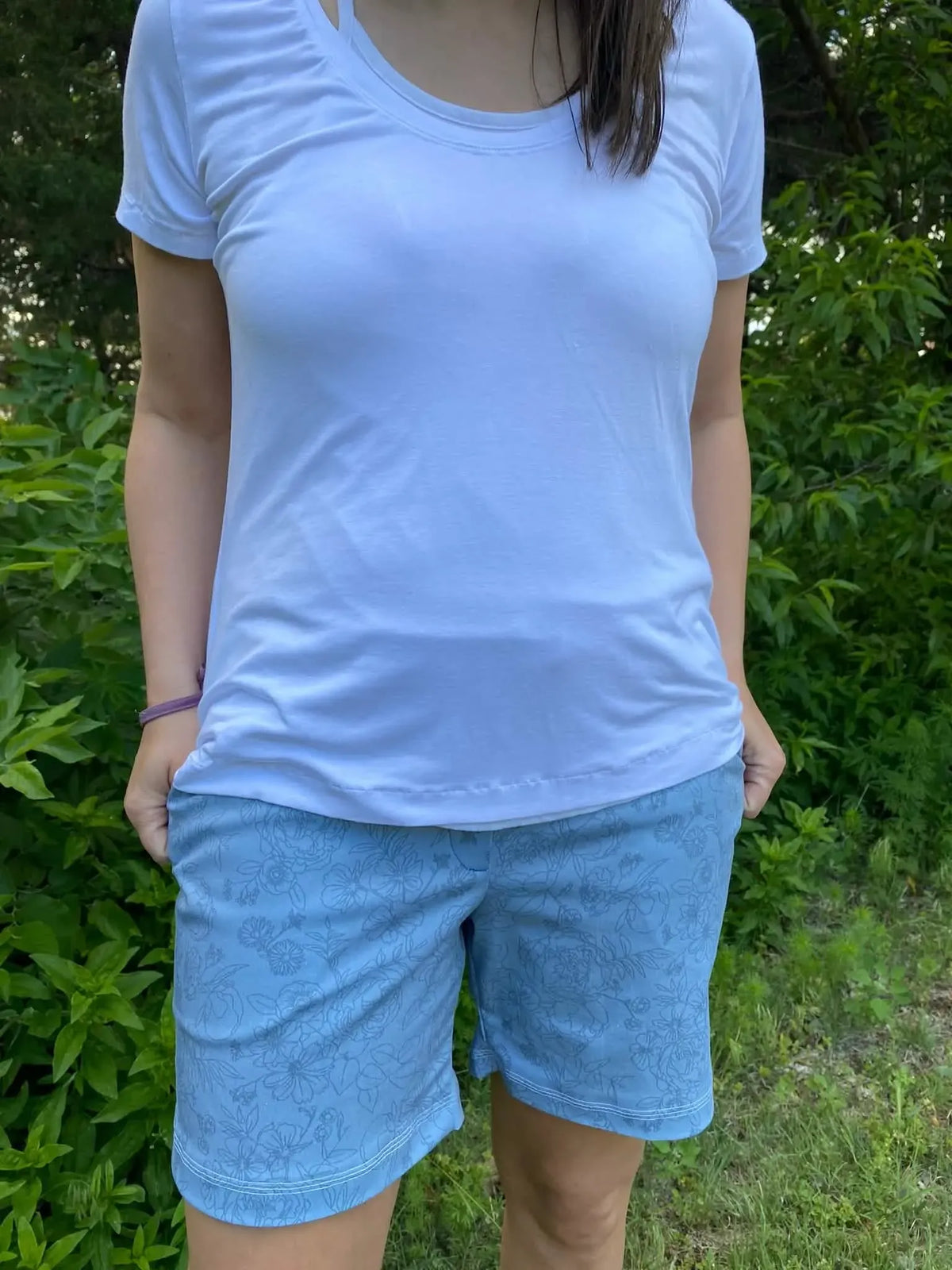 A person wears a white t-shirt and dusty blue stenciled floral shorts.