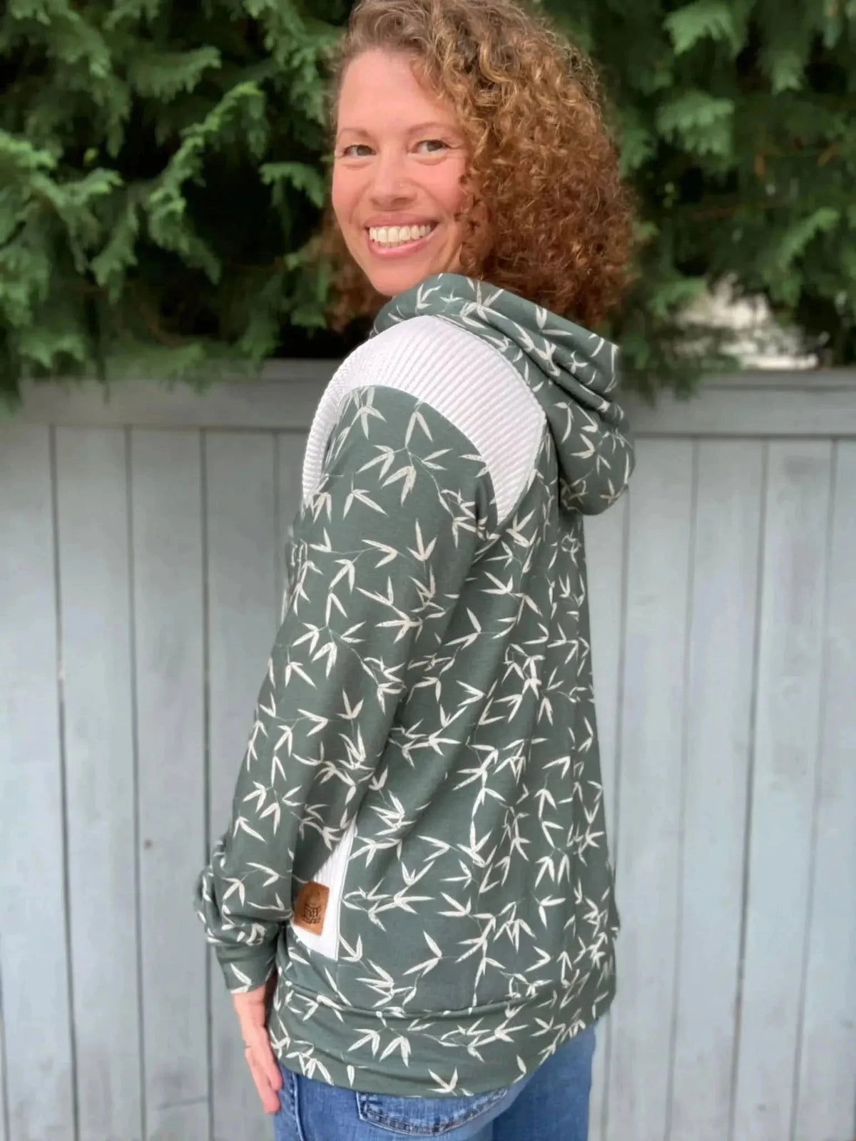 Woman modeling a green hooded sweatshirt with bamboo leaf print and white accents.