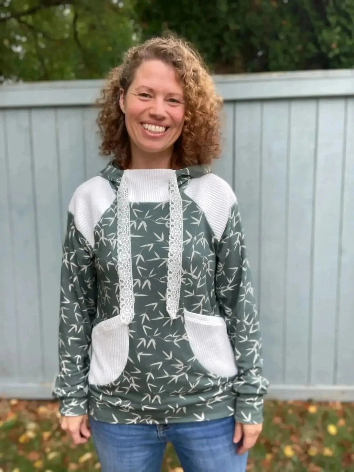 Woman wearing a green hoodie with white accents and bamboo leaf print, standing outdoors.