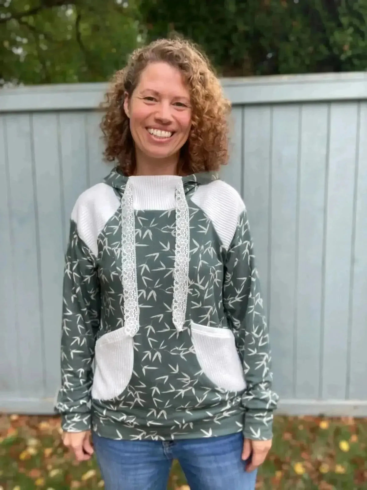 Woman wearing a green hoodie with white accents and bamboo leaf print, standing outdoors.
