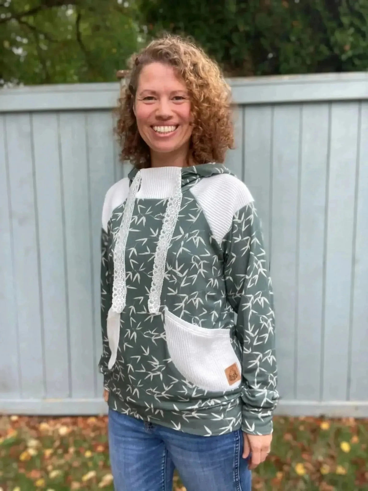 Woman wearing a green hoodie with white accents and bamboo leaf print, standing outdoors.