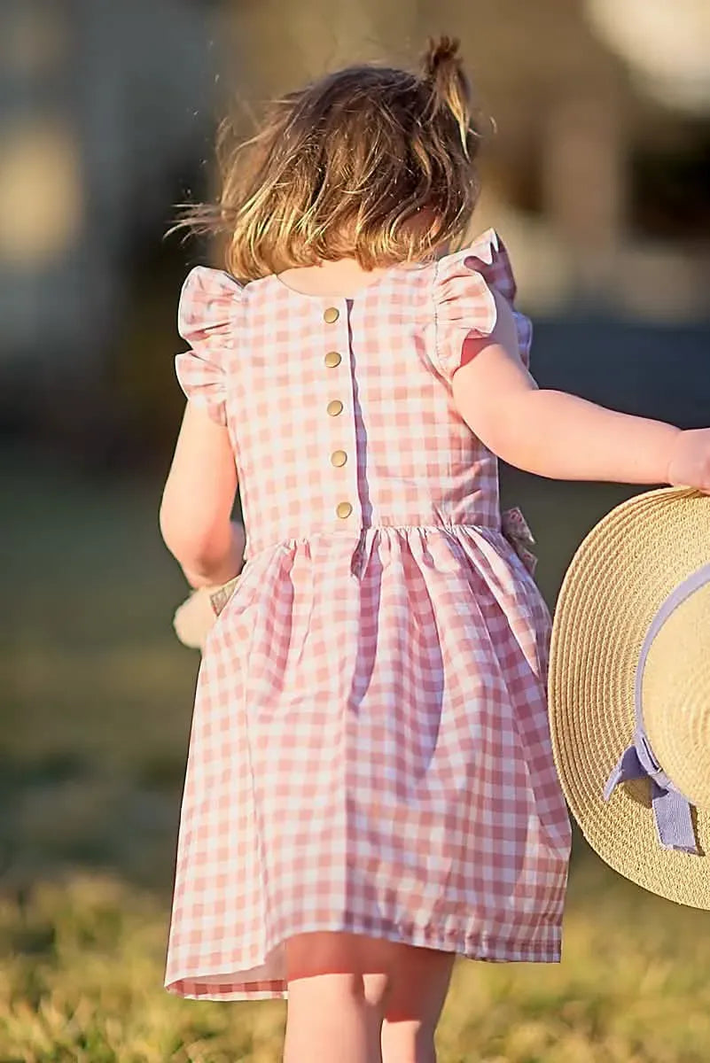 A child from behind wears a tan gingham dress with ruffled sleeves and gold buttons.