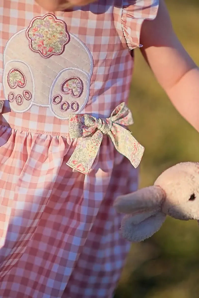 A child in a tan gingham dress with a bunny appliqué and a floral bow.