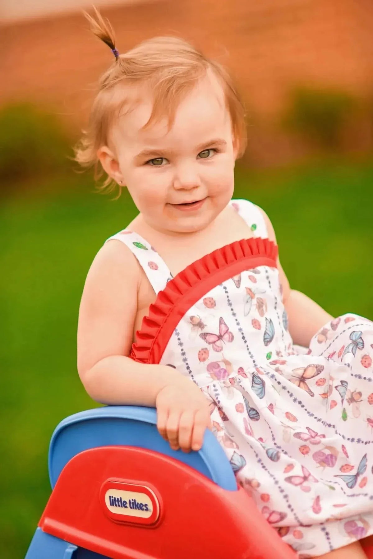 Toddler in a butterfly and bug print dress on a red and blue slide.