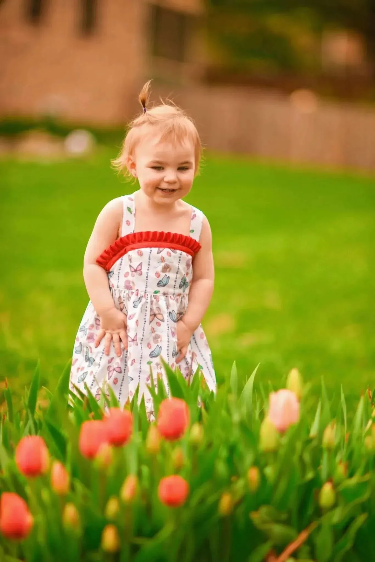 A smiling toddler in a white dress with red trim and butterfly print.
