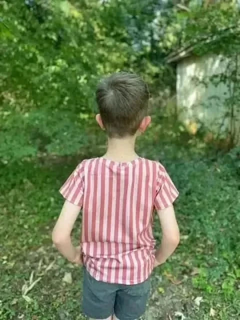 Boy wearing a red-and-white striped shirt made from Earthen Path fabric, viewed from behind in a wooded area.