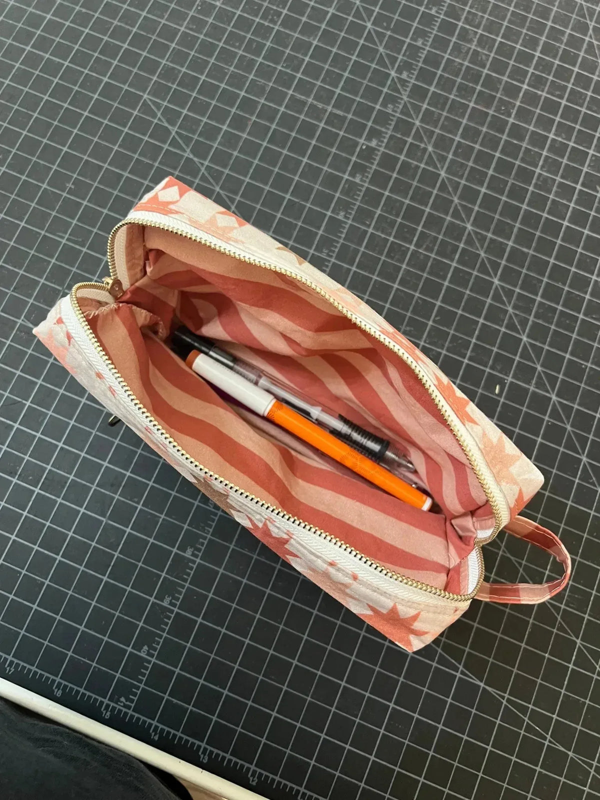 Open striped fabric pouch in neutral warm tones with star patterns, holding pens.