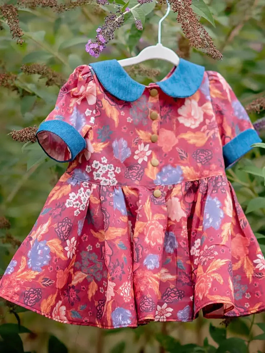 A floral print dress with a blue collar and cuffs hangs on a white hanger outdoors.