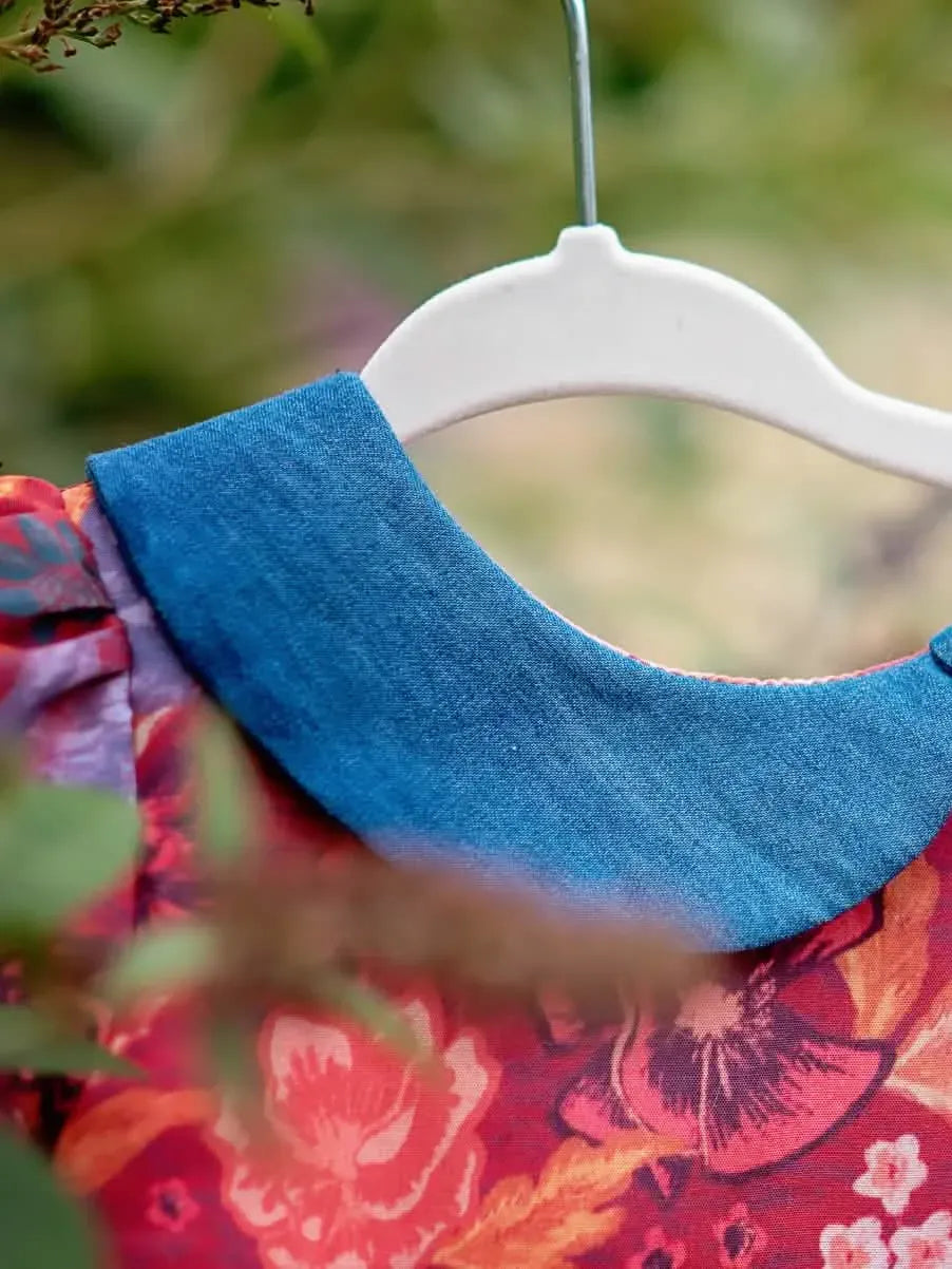 A red floral dress with a blue collar hangs on a white hanger outdoors.