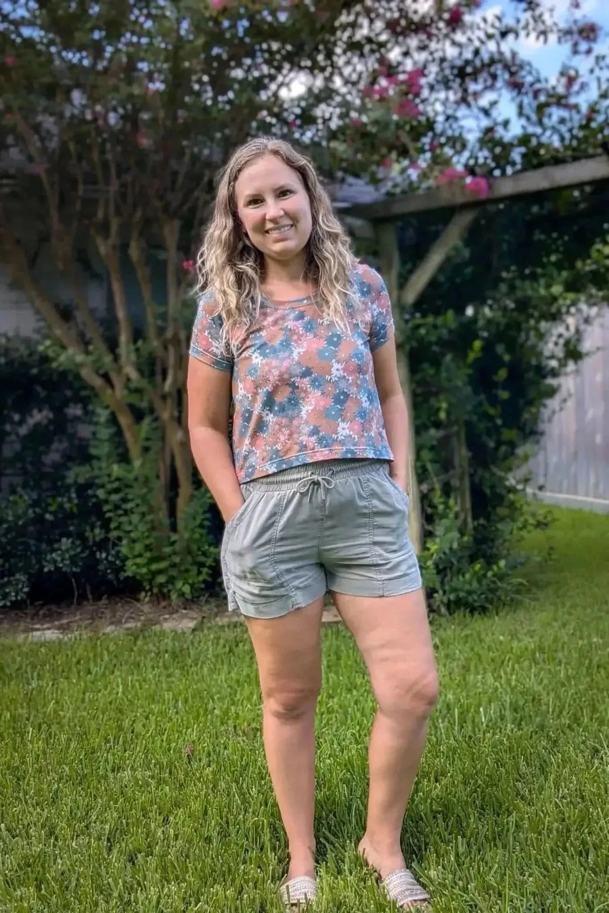 Woman wearing a floral print top and matching drawstring shorts in a garden.