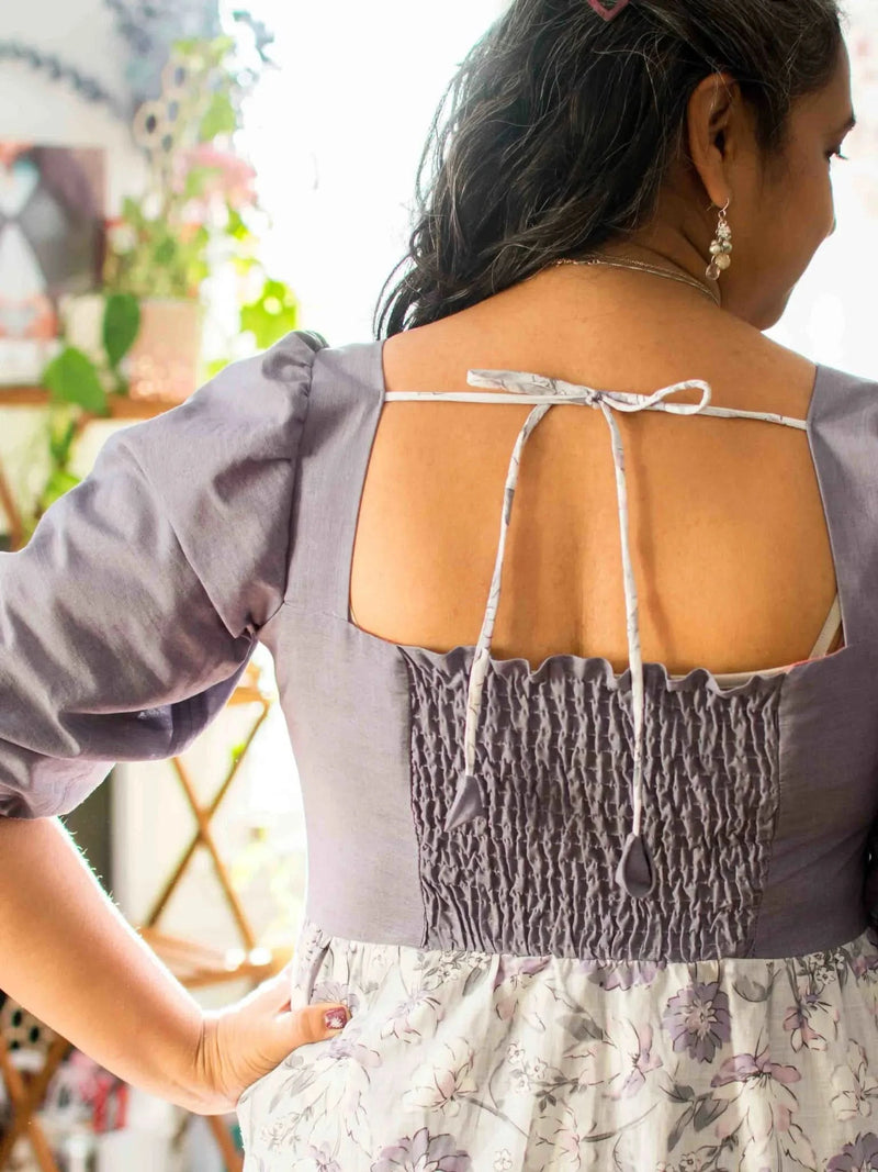 A woman from behind wearing a faded purple linen dress with floral print.