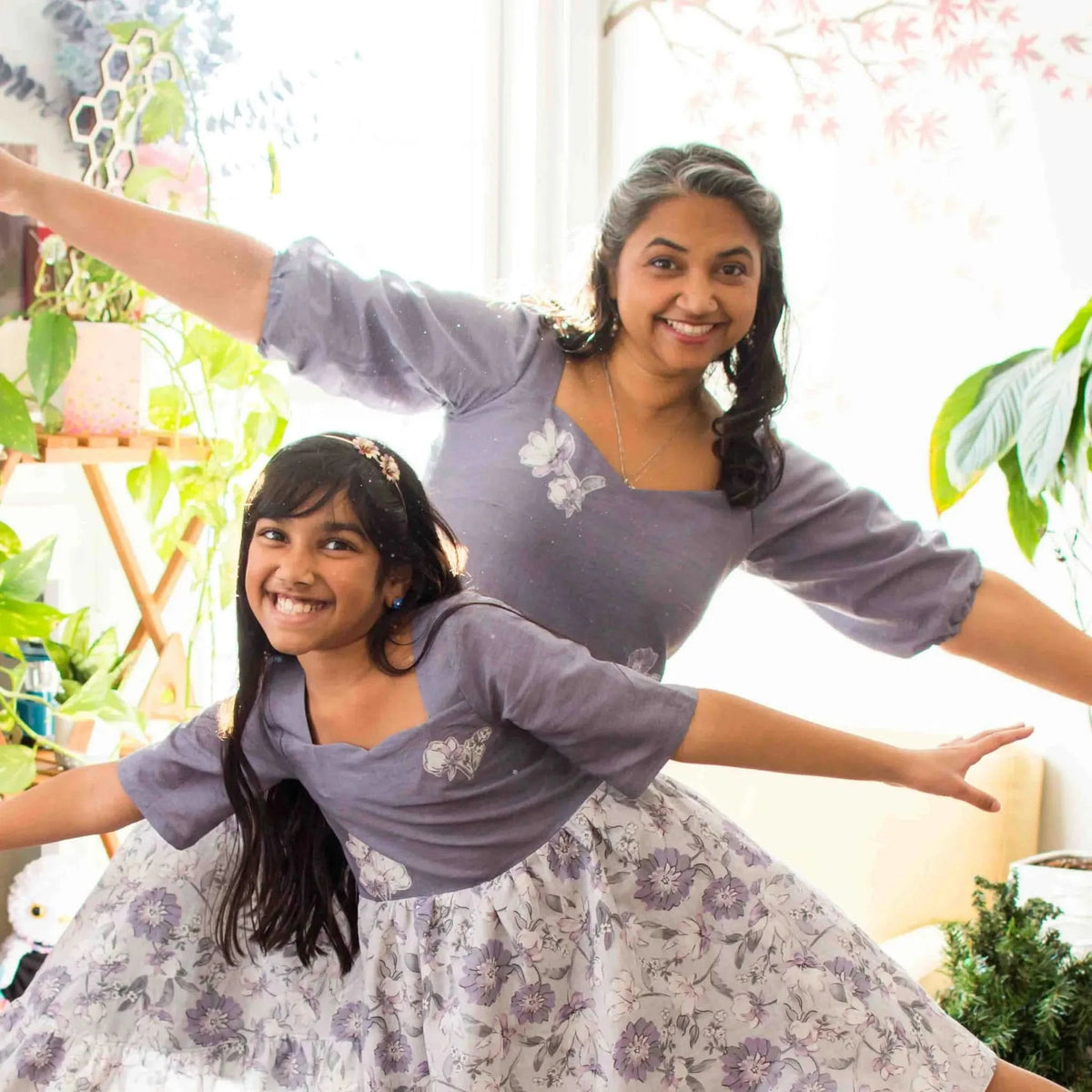 Two women in faded purple linen dresses with floral patterns.