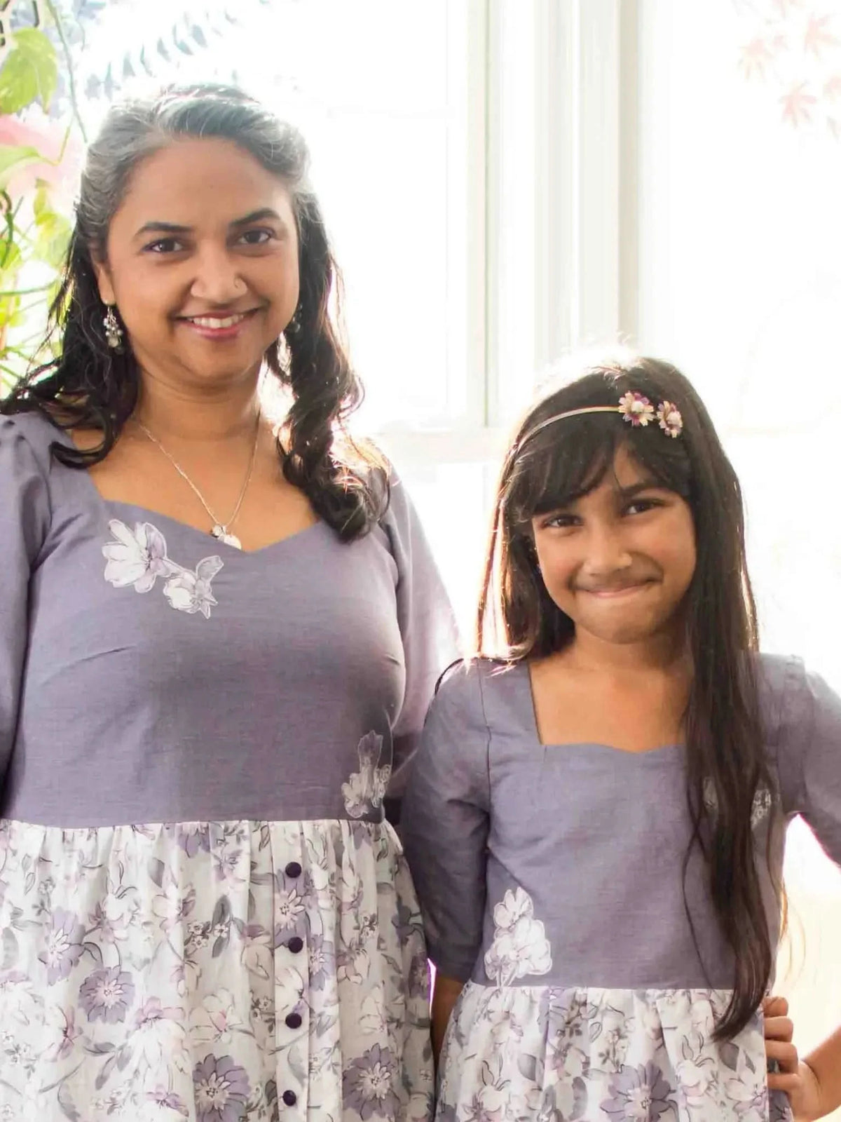 Two women in matching faded purple linen dresses with floral skirts.