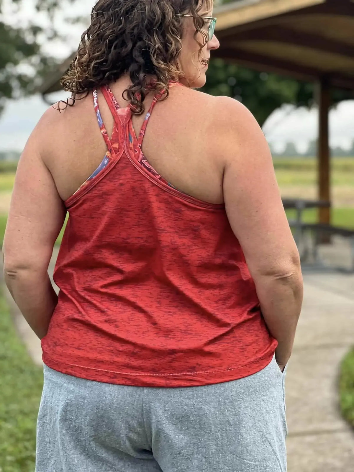 A person from behind wearing a red heather tank top and gray shorts.