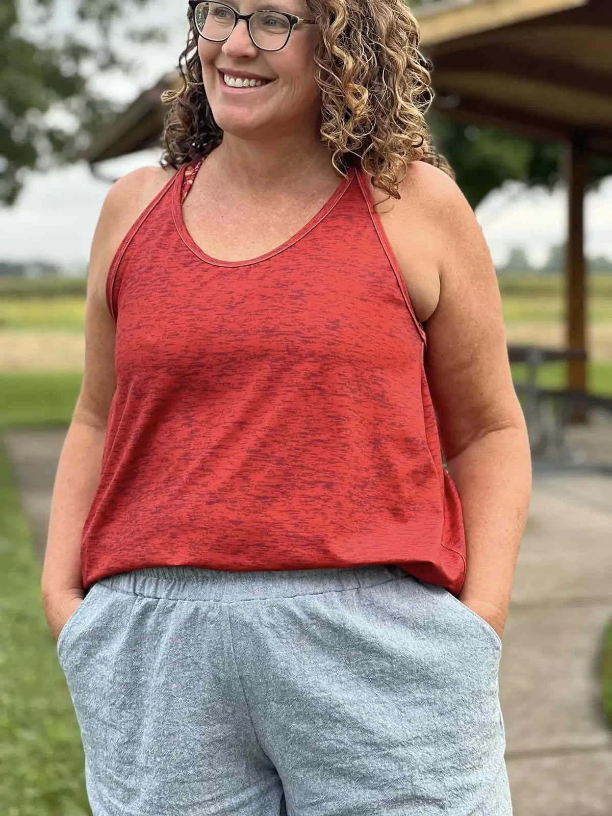 A woman wears a red heather tank top and gray shorts.