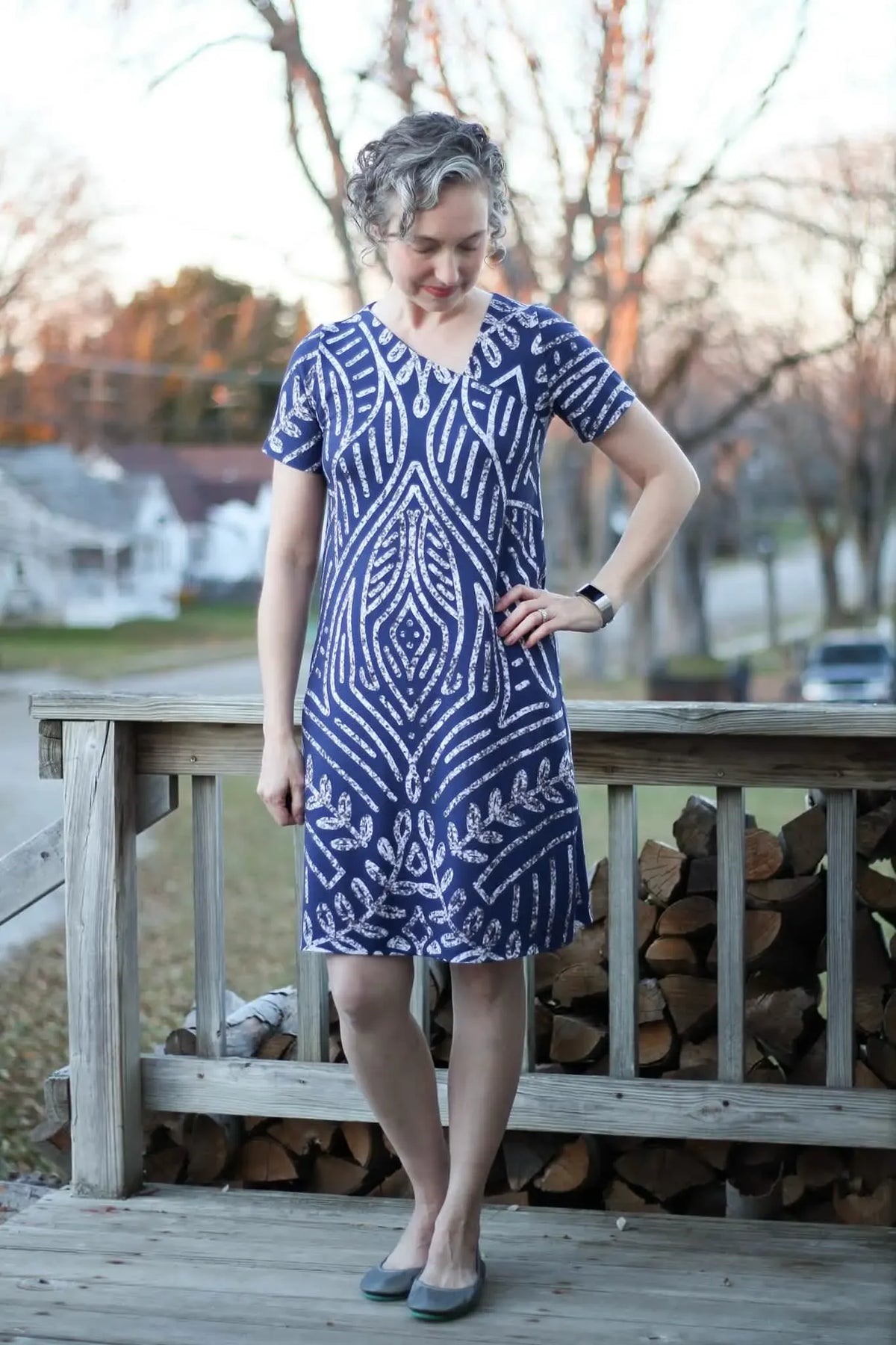 A woman in a blue and white patterned dress stands on a wooden porch.