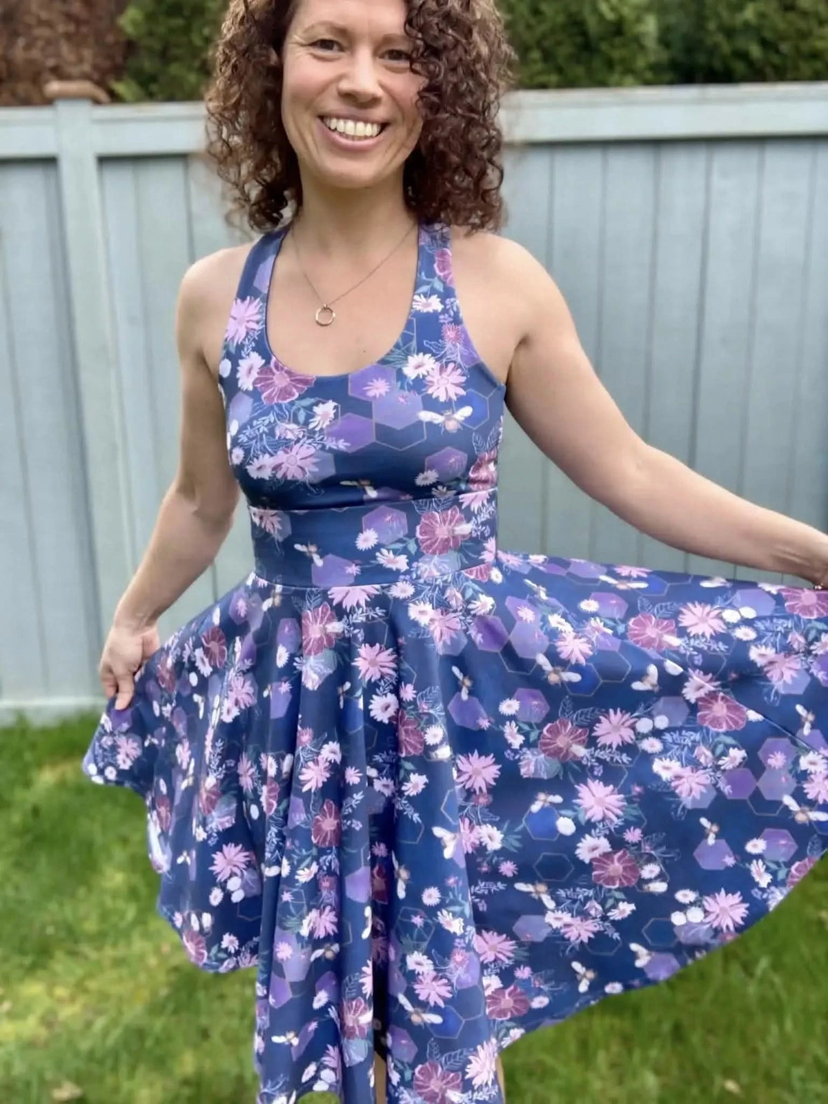 A woman smiles wearing a navy dress with purple flowers and bees.