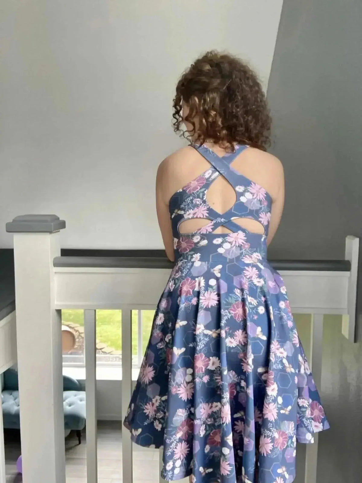 Rear view of a purple floral dress with crisscross back straps on a model.