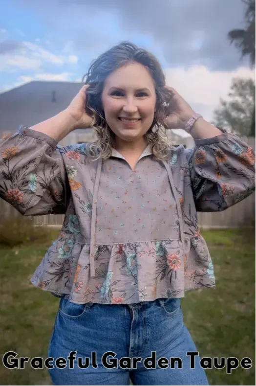 A woman smiles, wearing a taupe floral top and blue jeans.