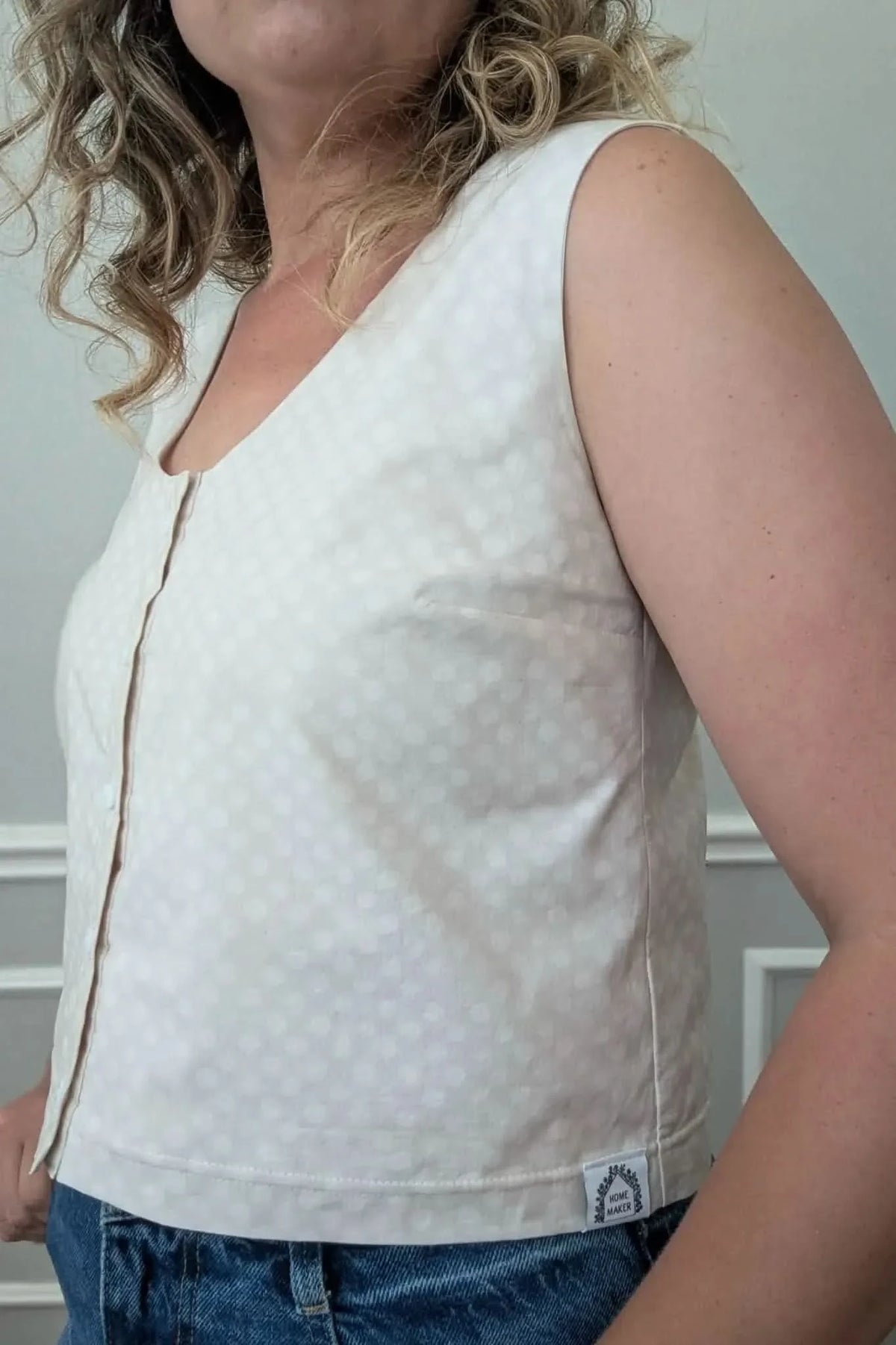 A woman wears a light beige polka dot sleeveless top with a button placket.