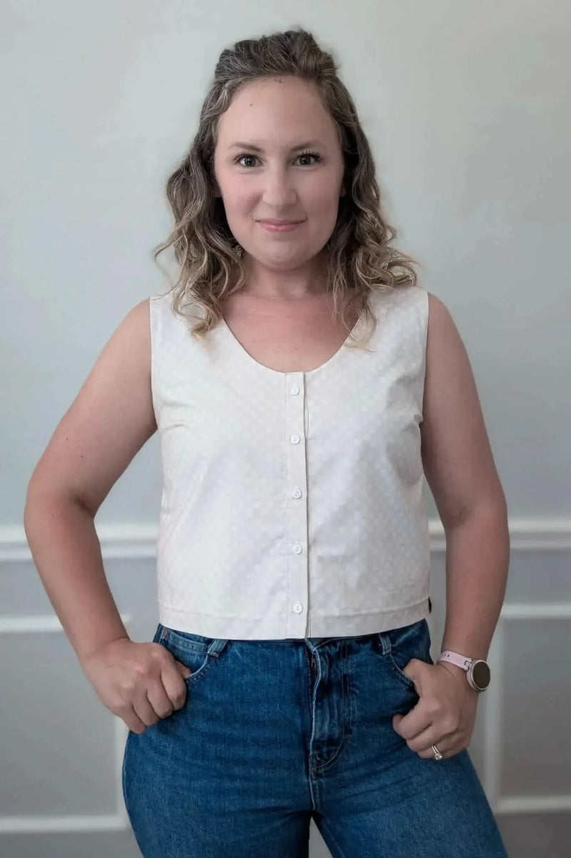 A woman models a sleeveless, button-front top with a subtle polka dot pattern and blue jeans.
