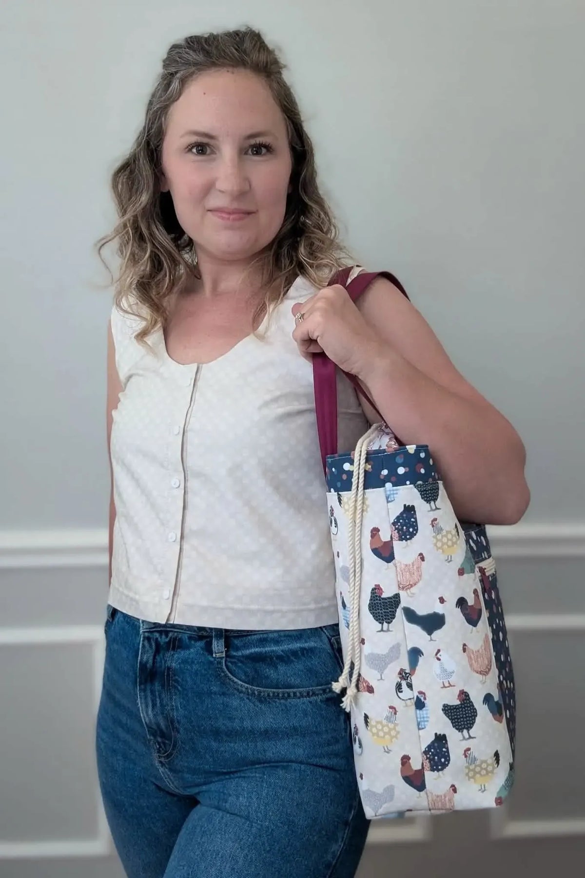 A woman holds a tote bag with a chicken pattern, wearing a polka dot top and jeans.