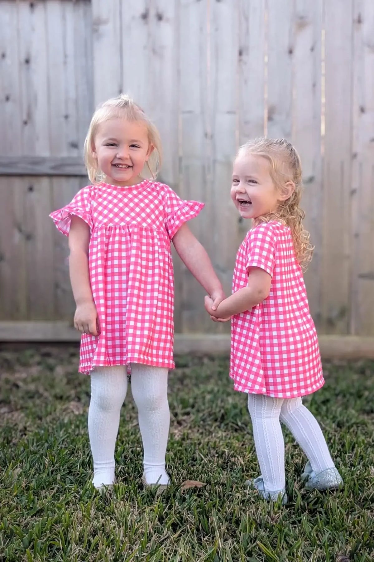 Two young girls wear hot pink gingham dresses and white tights.
