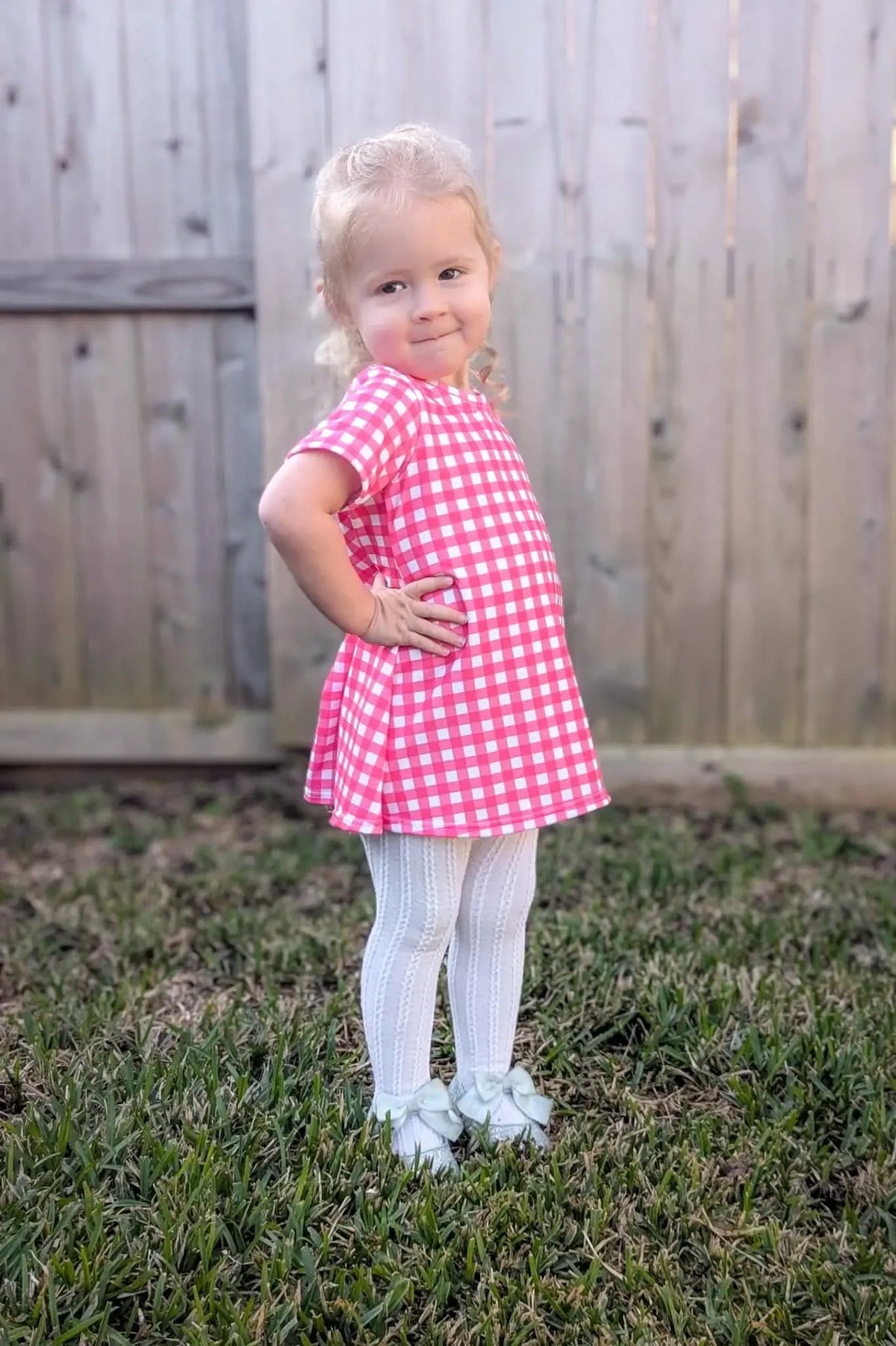 A young girl in a hot pink gingham dress, white tights, and light blue bow shoes.