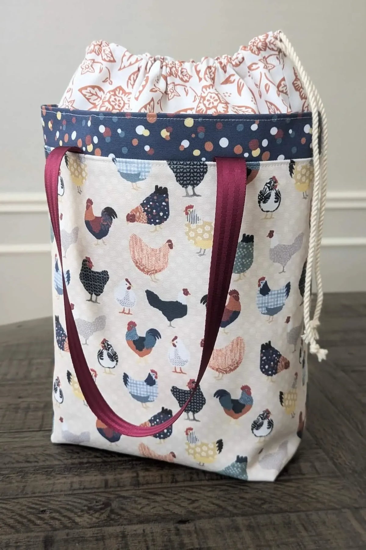 A fabric tote bag with a patchwork chicken pattern and a drawstring top.