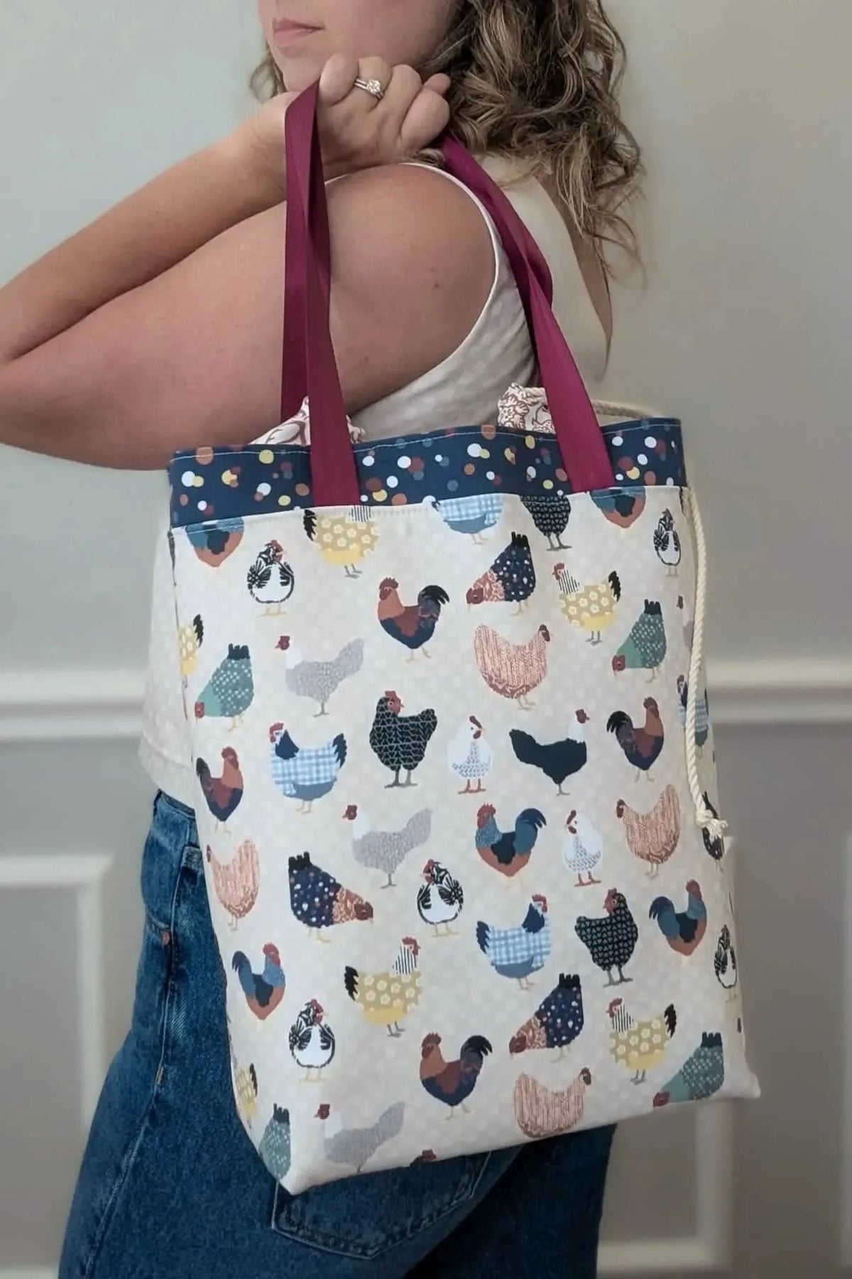 A person holds a tote bag with a patchwork chicken pattern.
