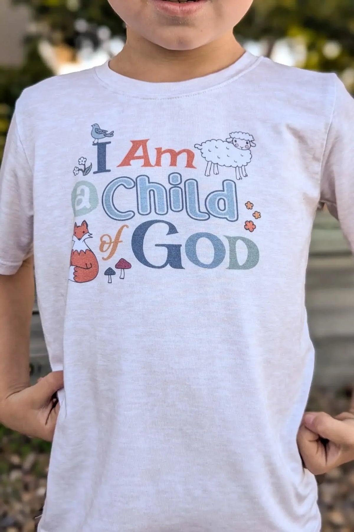 A child wears a light heathered t-shirt with "I Am a Child of God" in colorful letters.
